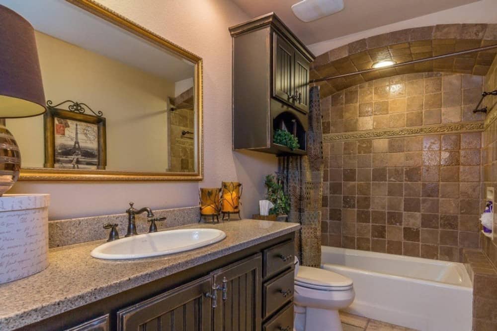 浴室有浴缸和淋浴组合，一个马桶，和一个洗手台梳妆台，上面有一面镀金镜子。