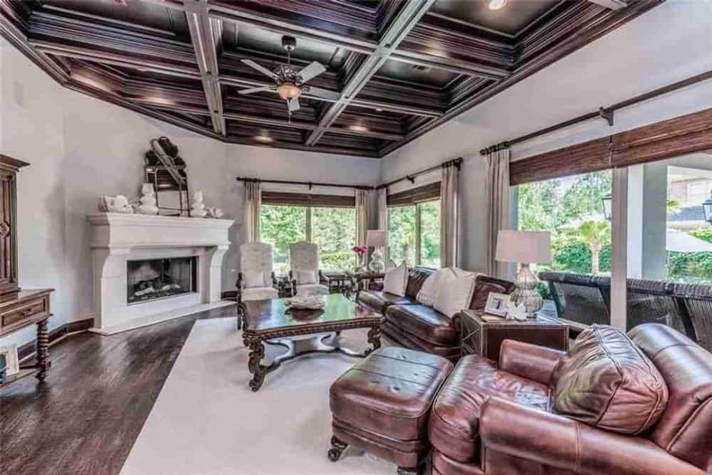 家庭娱乐室，带壁炉，真皮座椅，格子天花板下有一张木制咖啡桌。