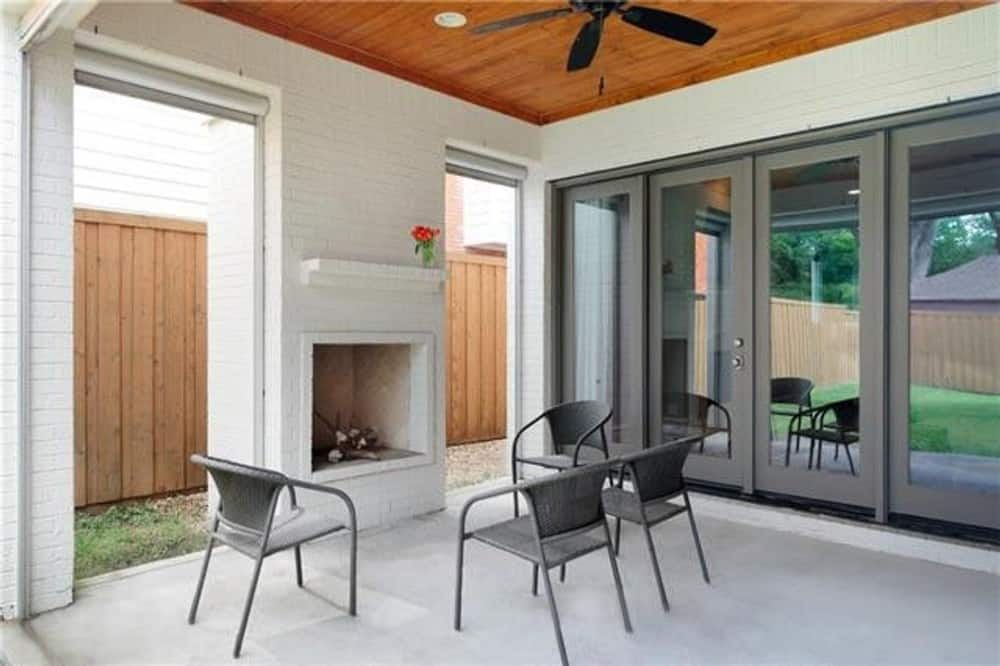 室外客厅里有金属椅子、一座壁炉和安装在木镶板天花板上的吊扇。