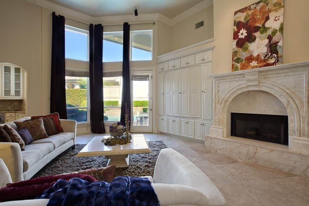 家庭娱乐室配有米色座椅，大理石壁炉，高高的窗户可以带来充足的自然光线。