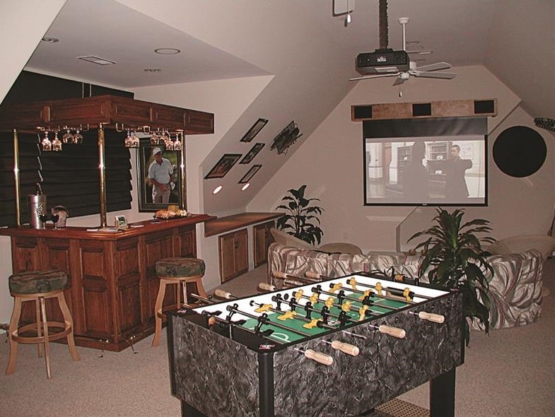 额外的房间有一张游戏桌，一个有图案的沙发，一个木制的吧台，和一个在拱形天花板下的屏幕投影仪。