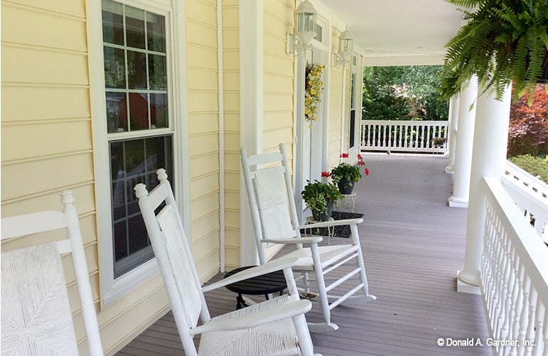 有顶棚的前廊上摆放着白色的摇椅，一个圆形的边桌，入口两侧的植物底座。