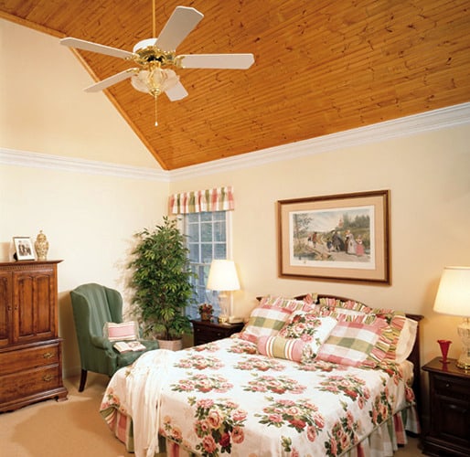 主卧室里有一张带裙的床、一张条纹的靠背椅子和一个覆盖着天然木材的拱形天花板。