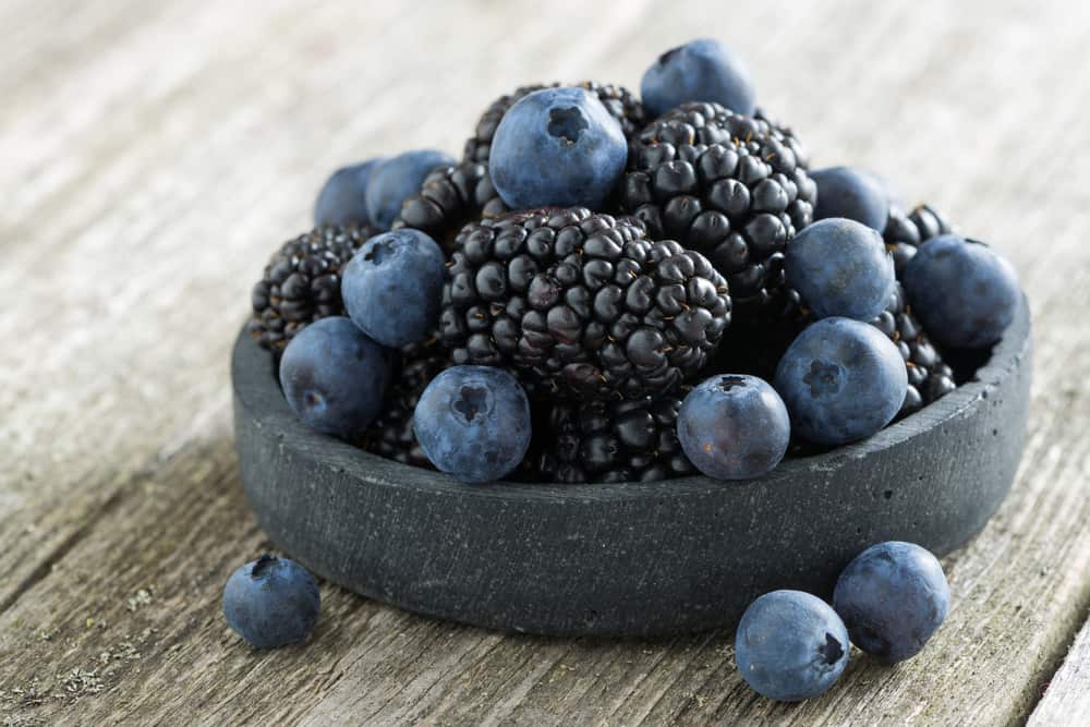 桌上放着一个装满黑莓和蓝莓的黑色小石碗。