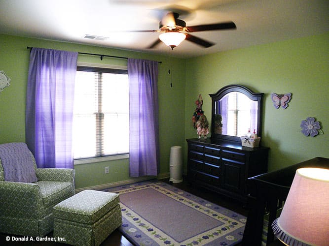 这间卧室有绿色的墙壁，一张有图案的躺椅，一个黑色的梳妆台，一扇挂着紫色窗帘的大窗户。