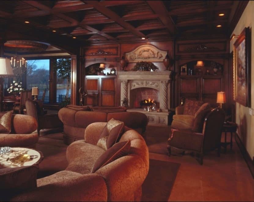 家庭娱乐室里有棕色座椅、一座壁炉和与格子天花板相匹配的木质嵌壁式家具。
