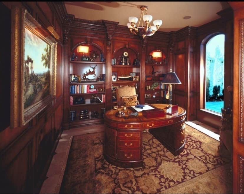 书房里摆满了嵌壁式书柜和一张椭圆形的桌子，桌子放在复古的小地毯上。