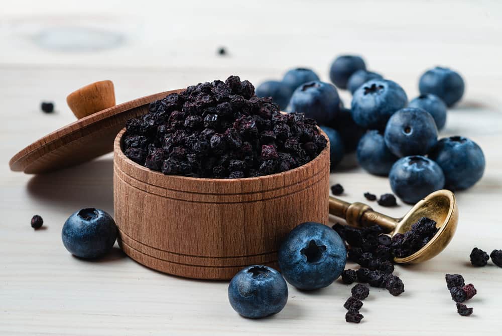 一种装有冷冻干燥蓝莓葡萄干的木制容器，旁边放着新鲜的蓝莓葡萄干。