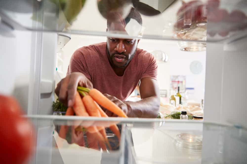一个男人把一串胡萝卜放进冰箱。