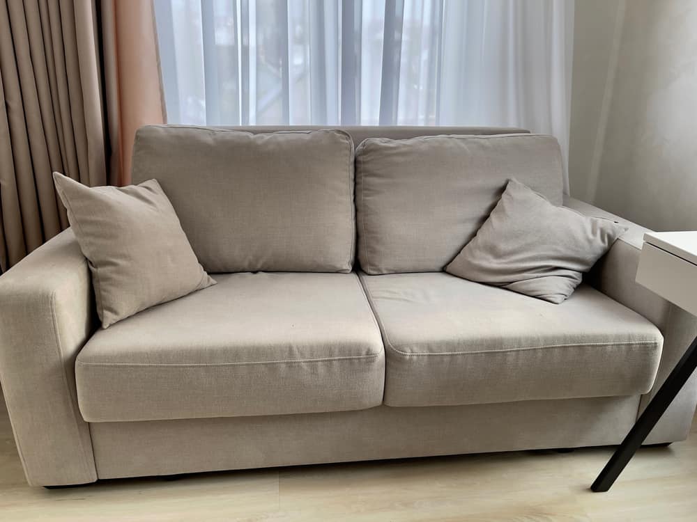 这是一张米色沙发，上面有厚厚的米色靠垫和枕头。