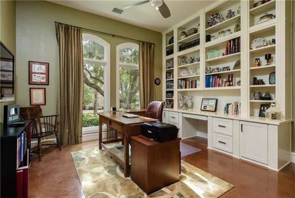书房里有白色的嵌壁式家具，一张木桌，高高的拱形窗户上挂着灰褐色的窗帘。