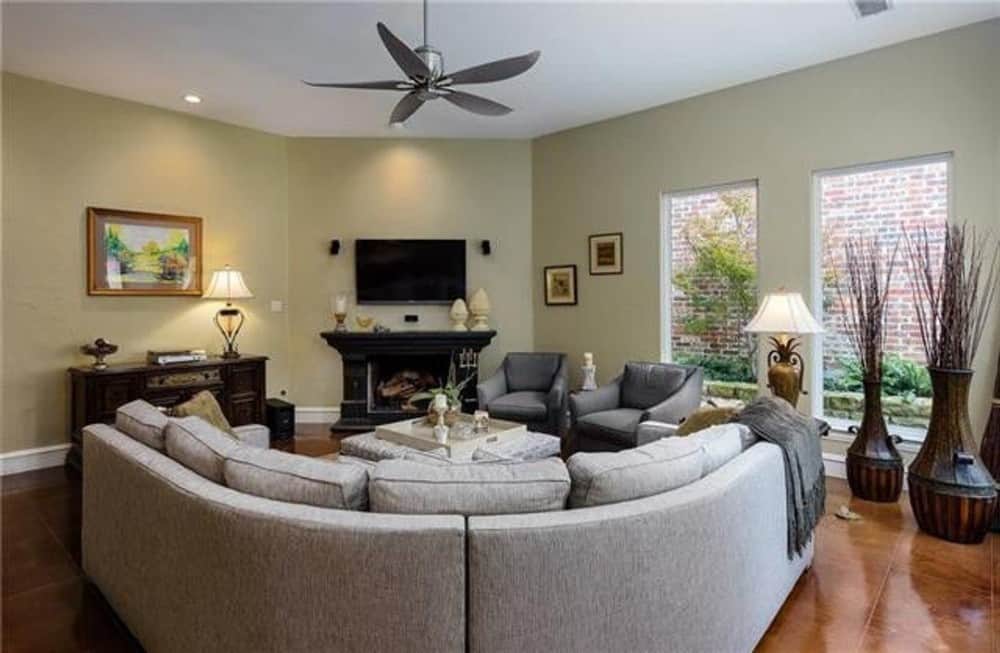 家庭娱乐室配有弧形沙发、灰色扶手椅，角落里有一座壁炉，壁炉顶部有一台电视。