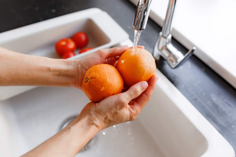 两个橙子正在厨房水龙头下手洗。