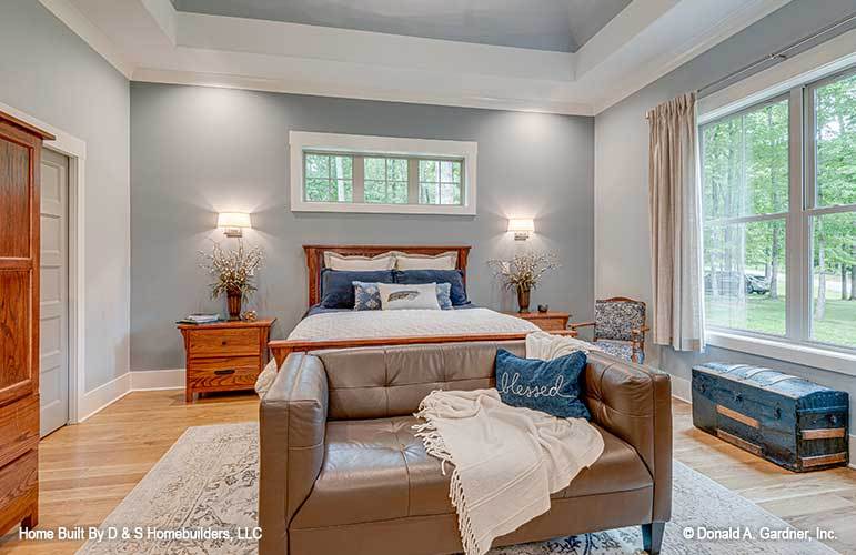 这间卧室有灰色的墙壁，一个箱子储物柜，一张木床和一张皮革簇绒双人沙发。