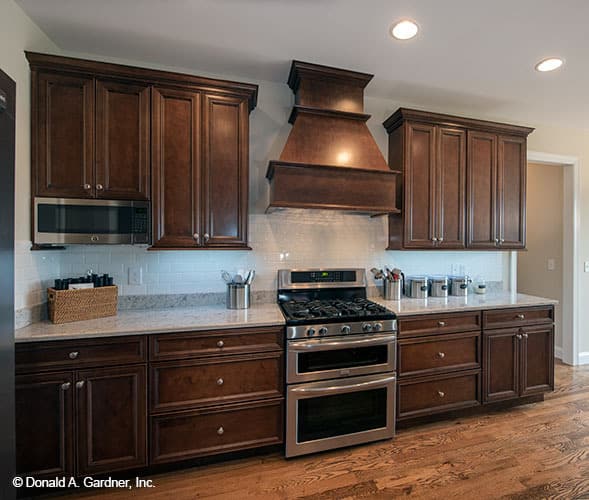 厨房配有深色木制橱柜，不锈钢烹饪灶，定制的通风罩固定在白色地铁瓷砖后挡板上。