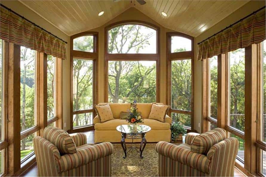 阳光房有拱形天花板、条纹扶手椅、米色沙发和一张圆形咖啡桌。