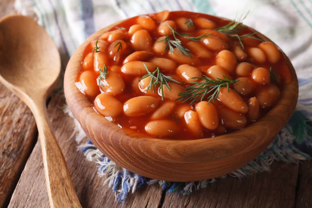 这是一个木碗，里面装满了番茄酱煮熟的豆子。