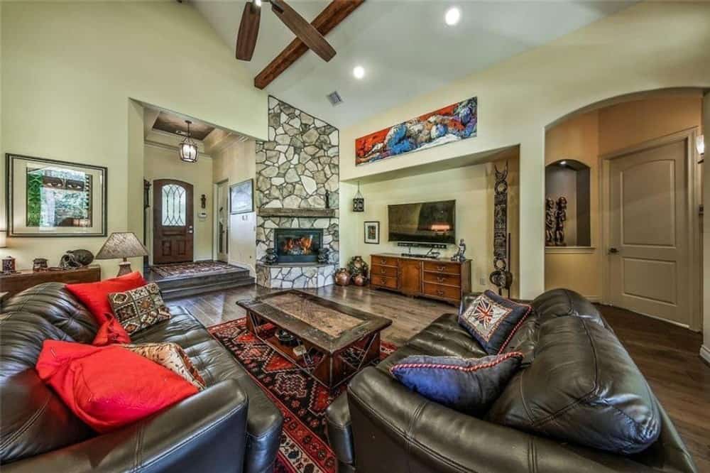 家庭娱乐室有黑色皮革沙发，木制咖啡桌，角落壁炉，电视安装在嵌壁上。