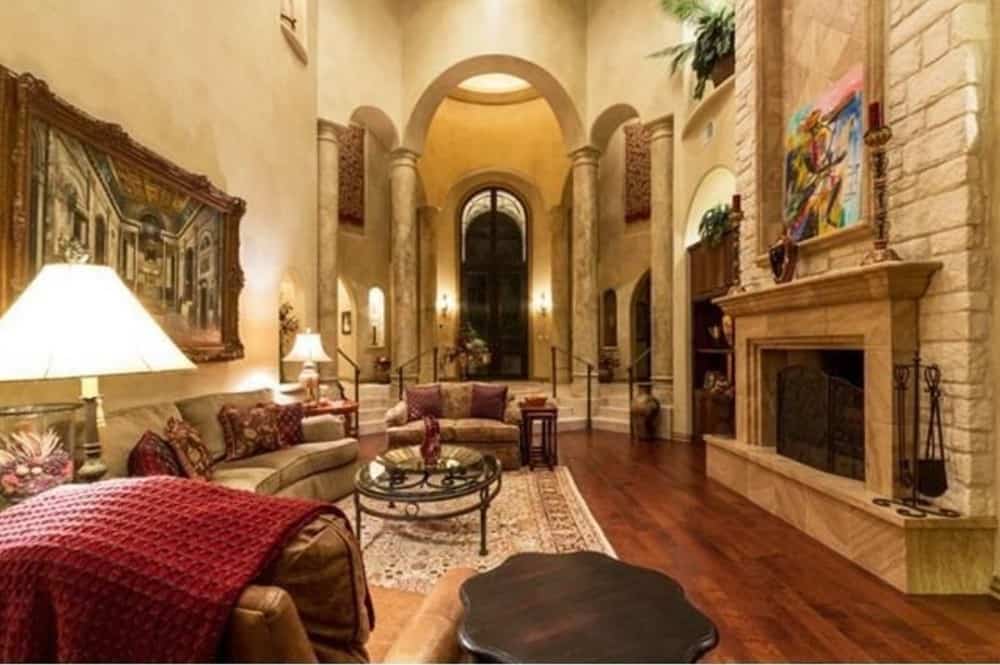 家庭娱乐室，有高耸的两层天花板，织物座椅和一个大壁炉，壁炉上装饰着一幅装裱好的画作。