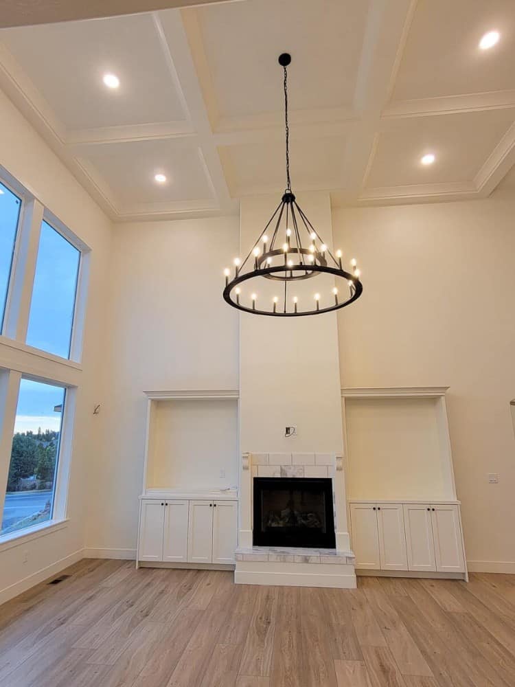大房间里有一个玻璃围起来的壁炉，白色的嵌壁式家具，高高的格子天花板上有一盏两层圆形吊灯。