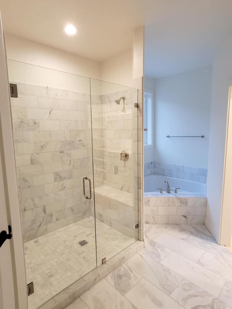主浴室包括一间步入式淋浴间和一间角落里铺着白色大理石瓷砖的浴缸。