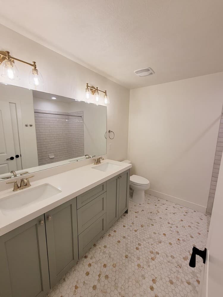 海克斯瓷砖地板和黄铜烛台突出了这个浴室。它有一个厕所和一个带双水槽的大梳妆台。