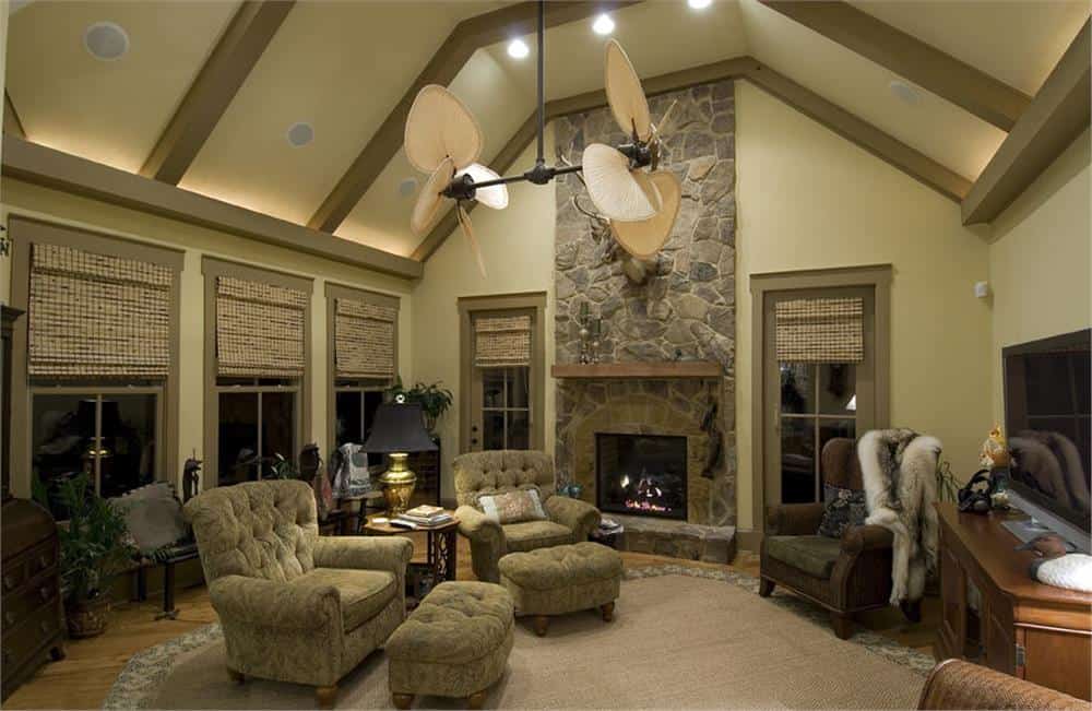 家庭娱乐室里有簇绒躺椅，拱形天花板下有一座石头壁炉，外露的横梁突出了壁炉的特色。