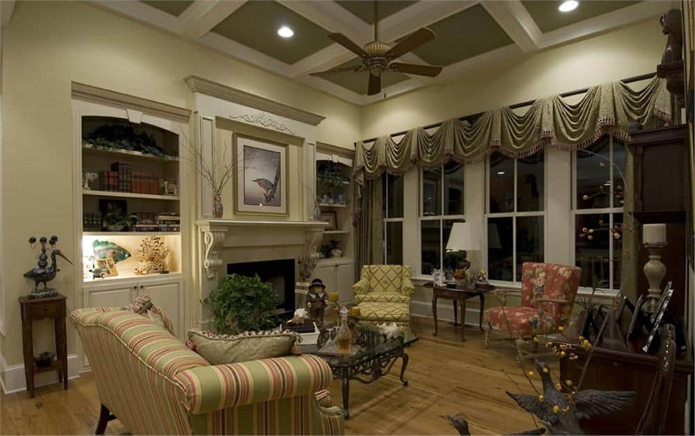 客厅里有格子天花板、有图案的座椅、一座壁炉和一面墙的窗户，窗户上装饰着优雅的帷幔。