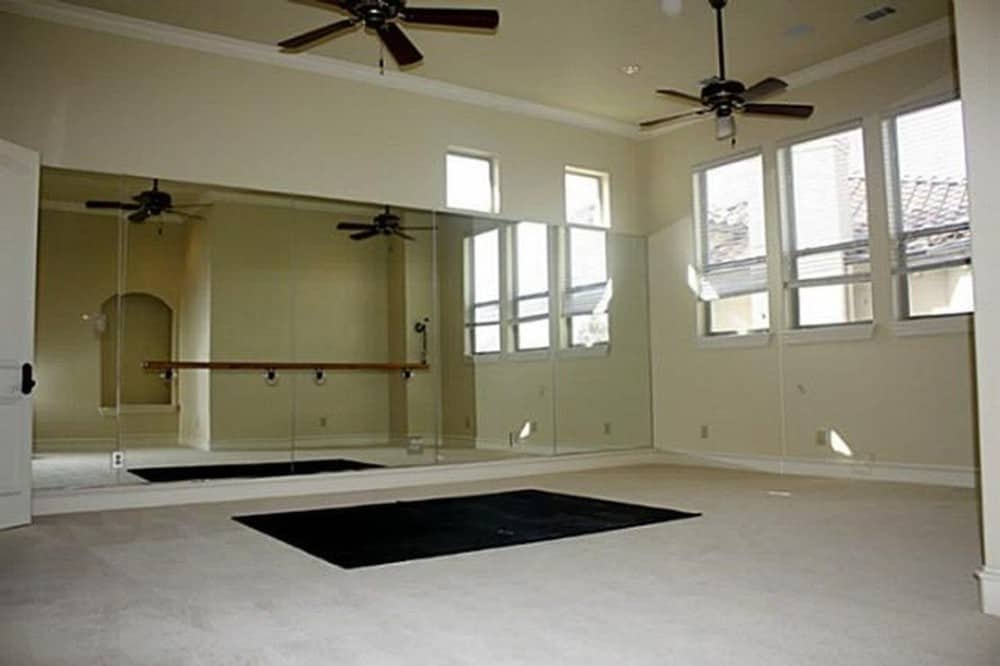 健身房有地毯地板，吊扇，还有一面墙的全身镜子。
