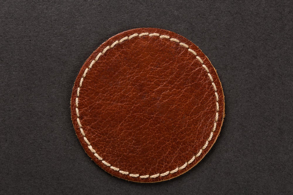 这是一个圆形的棕色皮革杯垫，侧面有缝线。