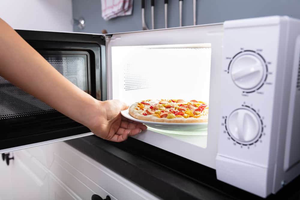 一个女人把冷冻披萨放进微波炉。