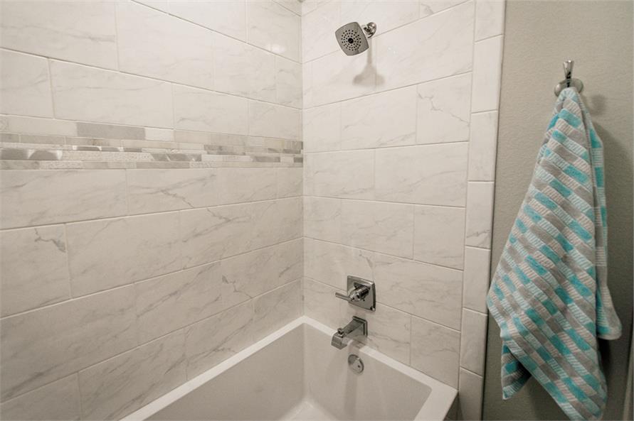 这间浴室配有浴缸和淋浴组合，配有铬固定装置和大理石瓷砖墙。