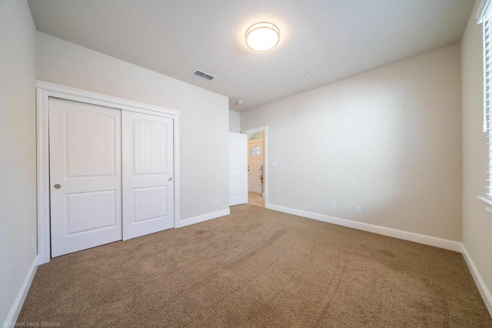 这间卧室有棚顶天花板，棕色地毯地板，还有一个嵌壁式衣柜，由白色滑动门封闭。