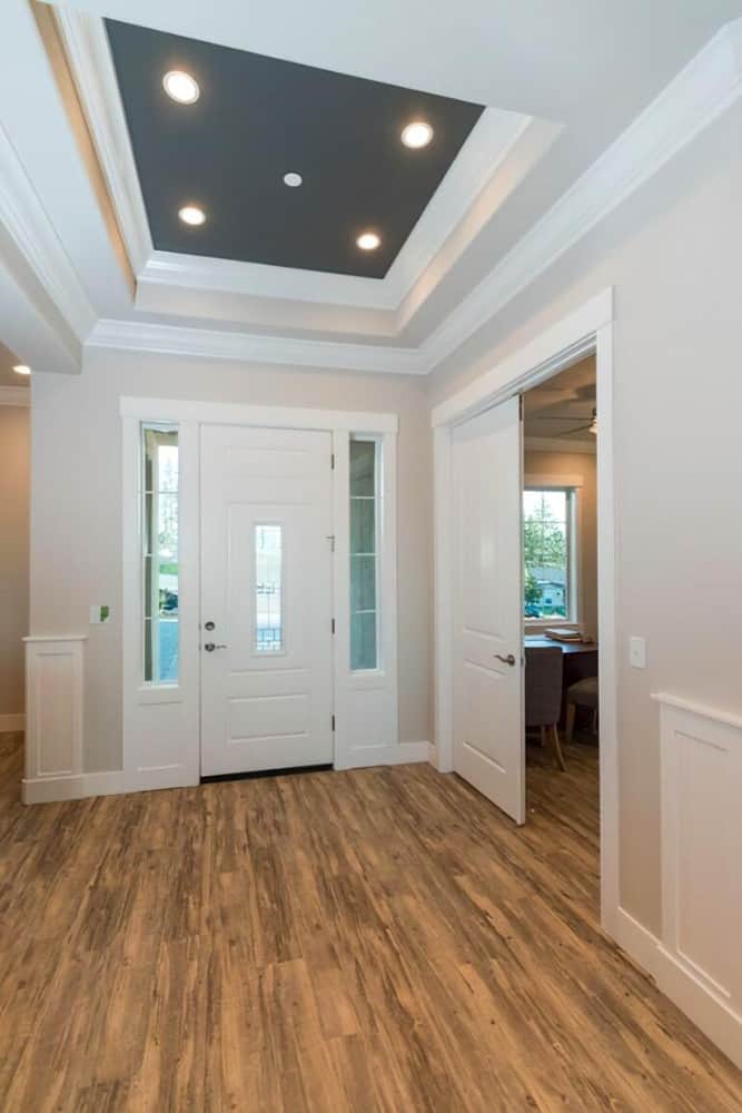 门厅有一个白色的入口门和一个灰色的托盘天花板，上面装有嵌入式灯。