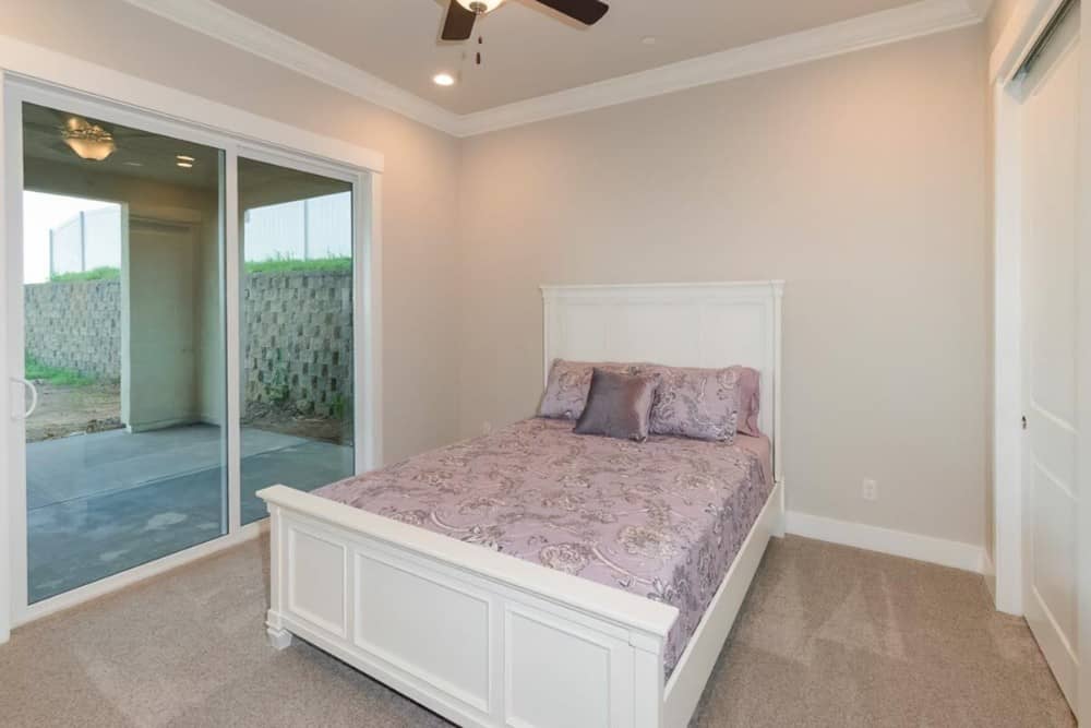 这间卧室铺着地毯，有一张白色的床，还有一扇通往后门廊的滑动玻璃门。