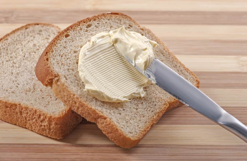 用黄油刀在木板上的小麦面包上涂黄油。