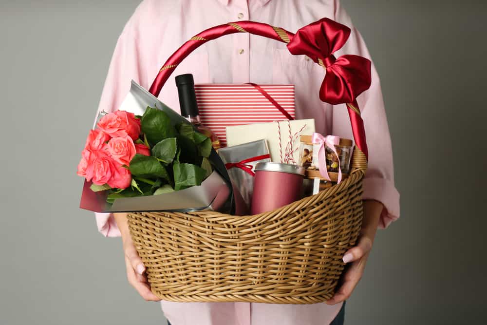 一个女人提着一个大柳条篮子，里面装满了玫瑰花、一瓶酒、糖果和礼物。