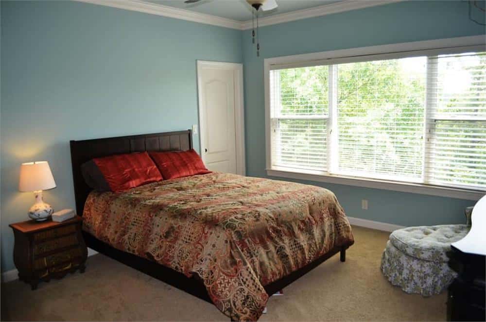 这间卧室里有一张深色的木床，一个簇绒躺椅，还有一扇大窗户，可以引入自然光。
