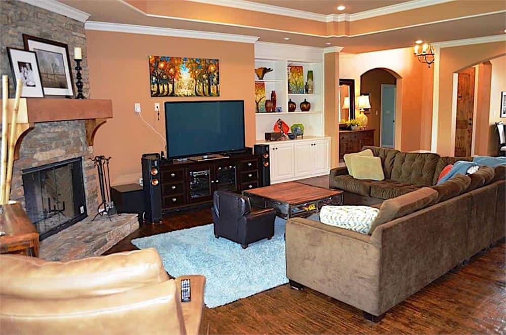 家庭娱乐室里有一座石砌壁炉、一台电视、l型沙发、真皮扶手椅和一个白色嵌壁式橱柜。