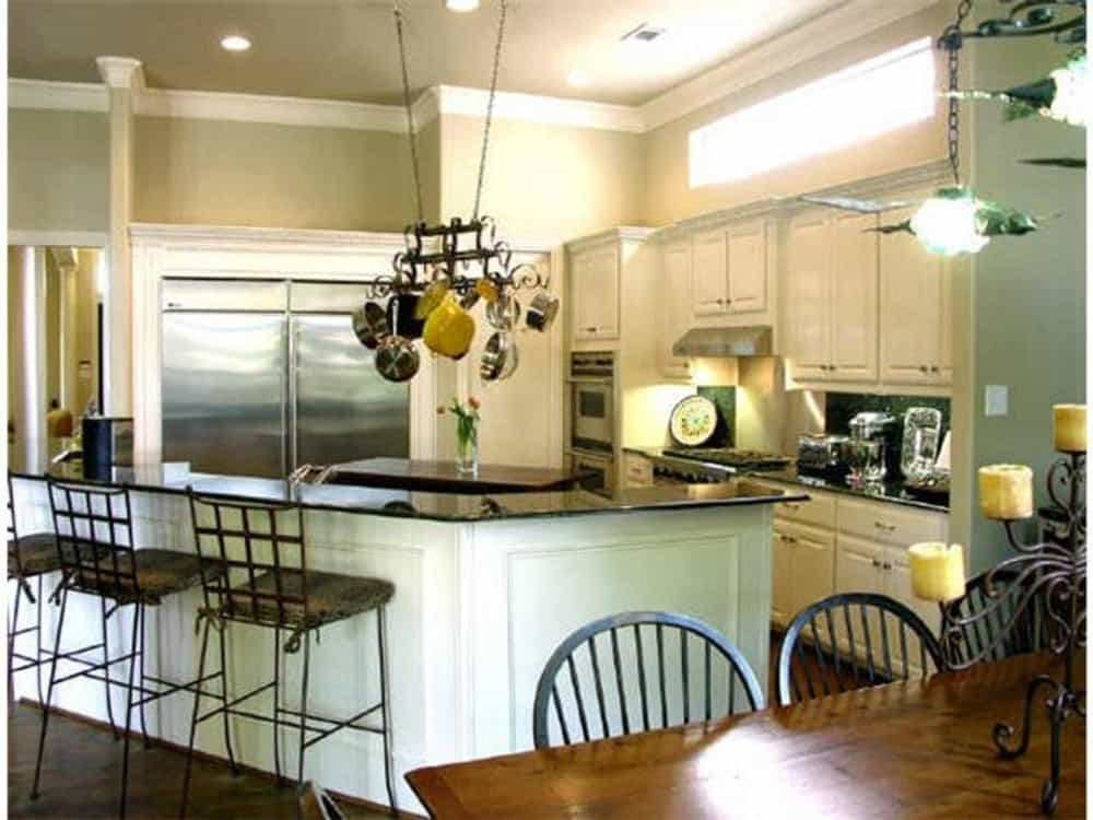 厨房配备了不锈钢器具、白色橱柜、倾斜的半岛和悬挂在中央岛台上的锅架。