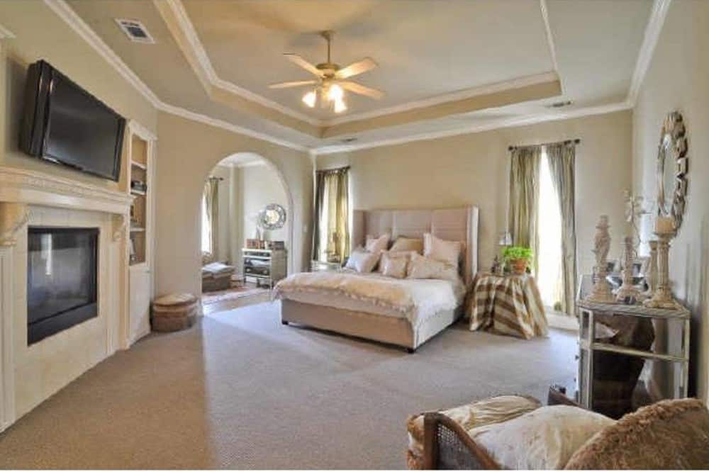 主卧室有一个托盘天花板，一个羽绒床，一个现代壁炉，和一个带拱门的坐角。