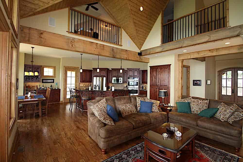 客厅里有皮革分割线，深色的木头咖啡桌放在有图案的区域地毯上。它的顶部有一个高高的拱形天花板，通往厨房和餐厅区。