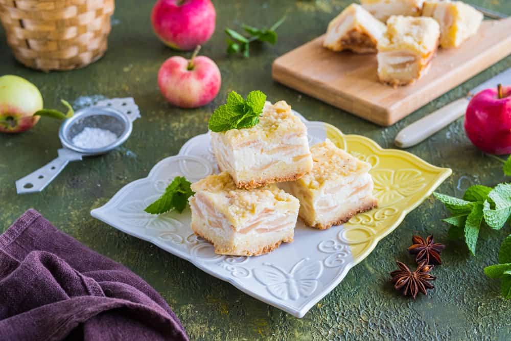 奶酪蛋糕苹果派倒挂在一个复杂的盘子上，放在绿色的水泥桌上，上面放着新鲜的苹果水果。