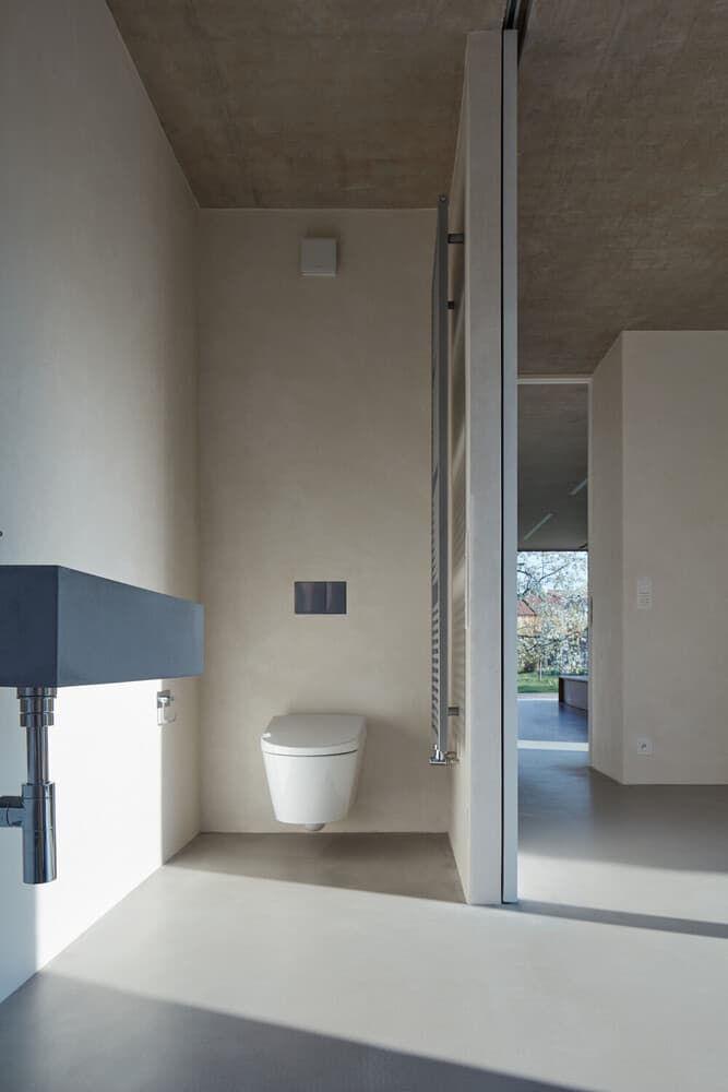 浴室有简单的白色墙壁，一个灰色的浮动梳妆台，远侧有一个厕所。