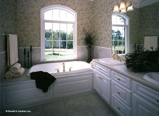 主浴室配有双洗手台和固定在拱形窗下的落地式浴缸。