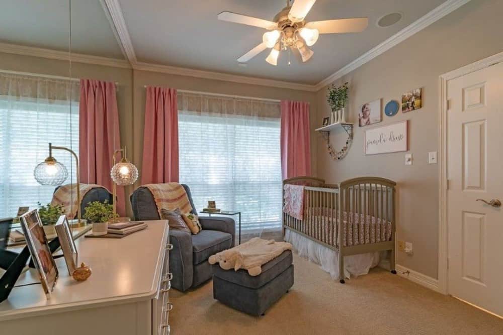 育婴室里有一个木制的婴儿床，灰色的躺椅，地毯地板上有一个白色的梳妆台。