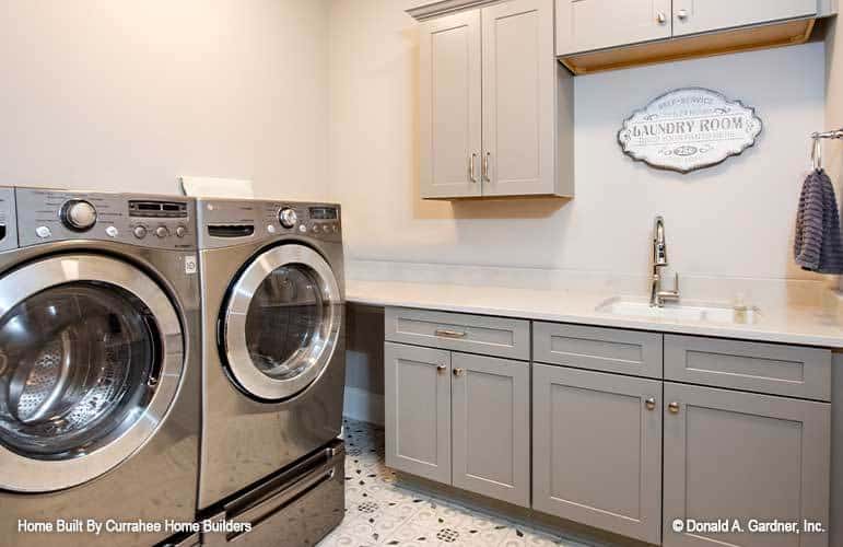 洗衣房配备了灰色的橱柜，一台前置洗衣机和烘干机，以及一个多功能水槽。