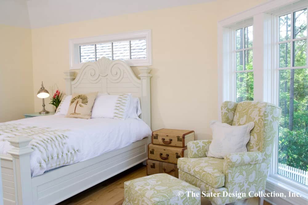 这间卧室有奶油色的墙壁、一张白色的床和一把带图案的靠背椅子，椅子上还有一个配套的软凳。