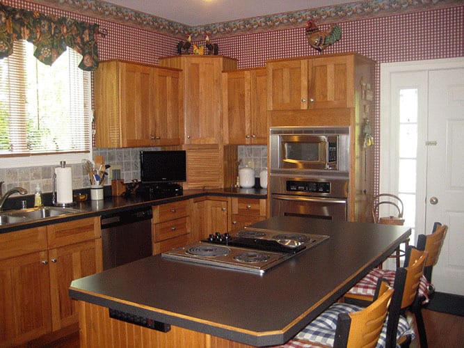 厨房配有黑色和不锈钢电器，木制橱柜，和一个配有软垫柜台椅的灶台岛。
