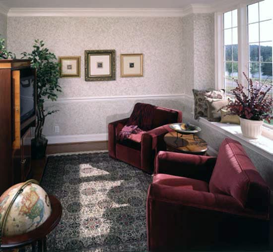 书房里有红色扶手椅，装饰着有图案的墙纸、装裱好的艺术品和新鲜的盆栽。